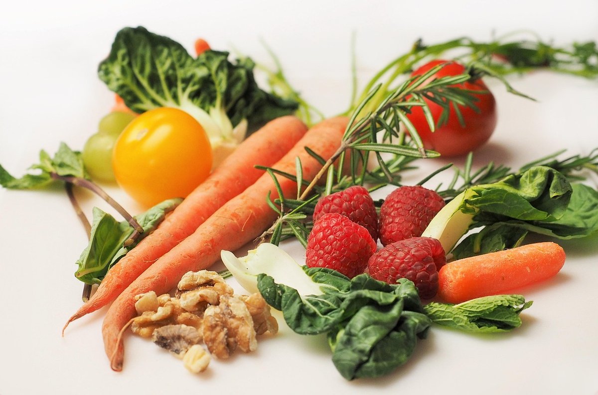 Carrots, spinach, tomatoes, raspberries and walnuts laid out on a white surface