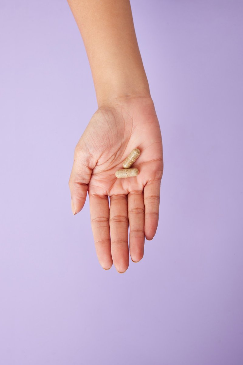Open hand holding two beige herbal supplement capsules against a lilac background